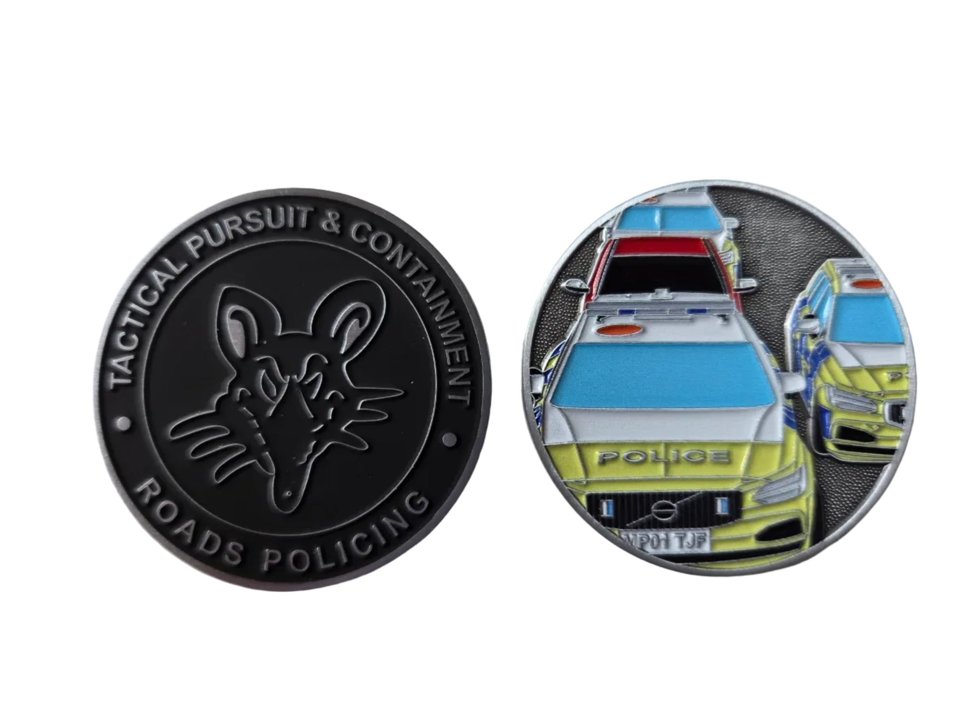 Two circular challenge coins on a light gray surface. The left coin is black with an embossed fox head and the text 'TACTICAL PURSUIT & CONTAINMENT' and 'ROADS POLICING'.
